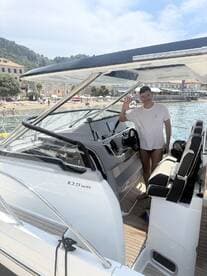 A man waves from the helm of a stylish boat, showcasing the modern interior design and seating area — perfect for navigating the open waters.