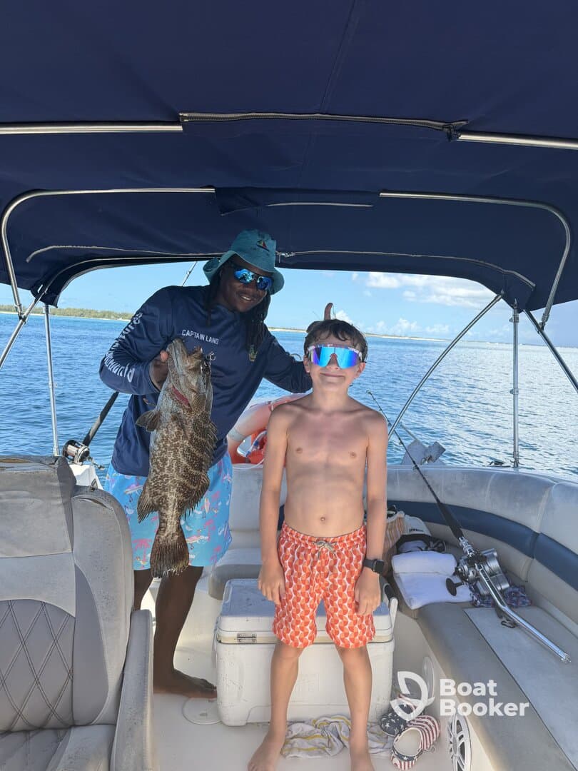 A young boy proudly poses with a large fish alongside his captain on a boat, capturing a memorable fishing experience on the water.