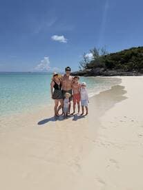 A joyful family poses together on a beautiful beach, surrounded by turquoise waters and soft sand — a perfect snapshot of their tropical vacation.