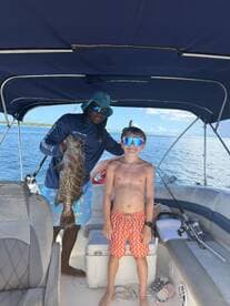 A young boy proudly poses with a large fish alongside his captain on a boat, capturing a memorable fishing experience on the water.