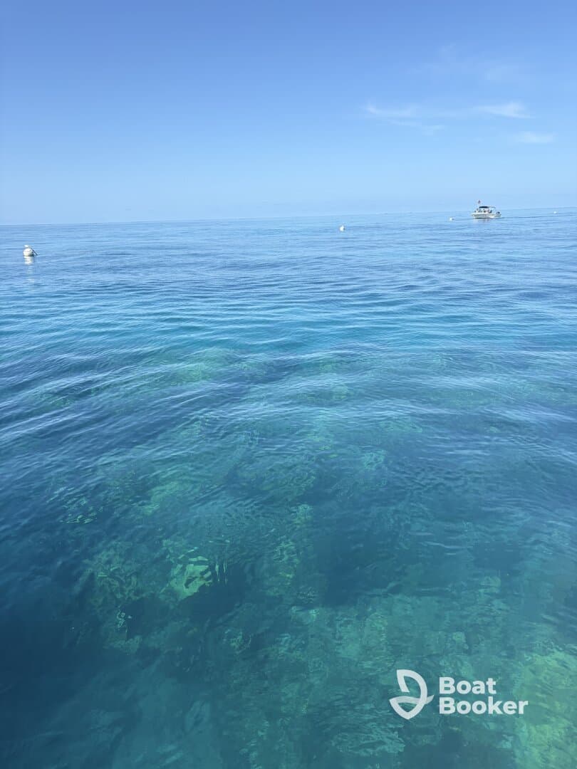 A serene view of clear turquoise waters, with a distant boat visible. The underwater features are partially obscured, making the scene less defined.