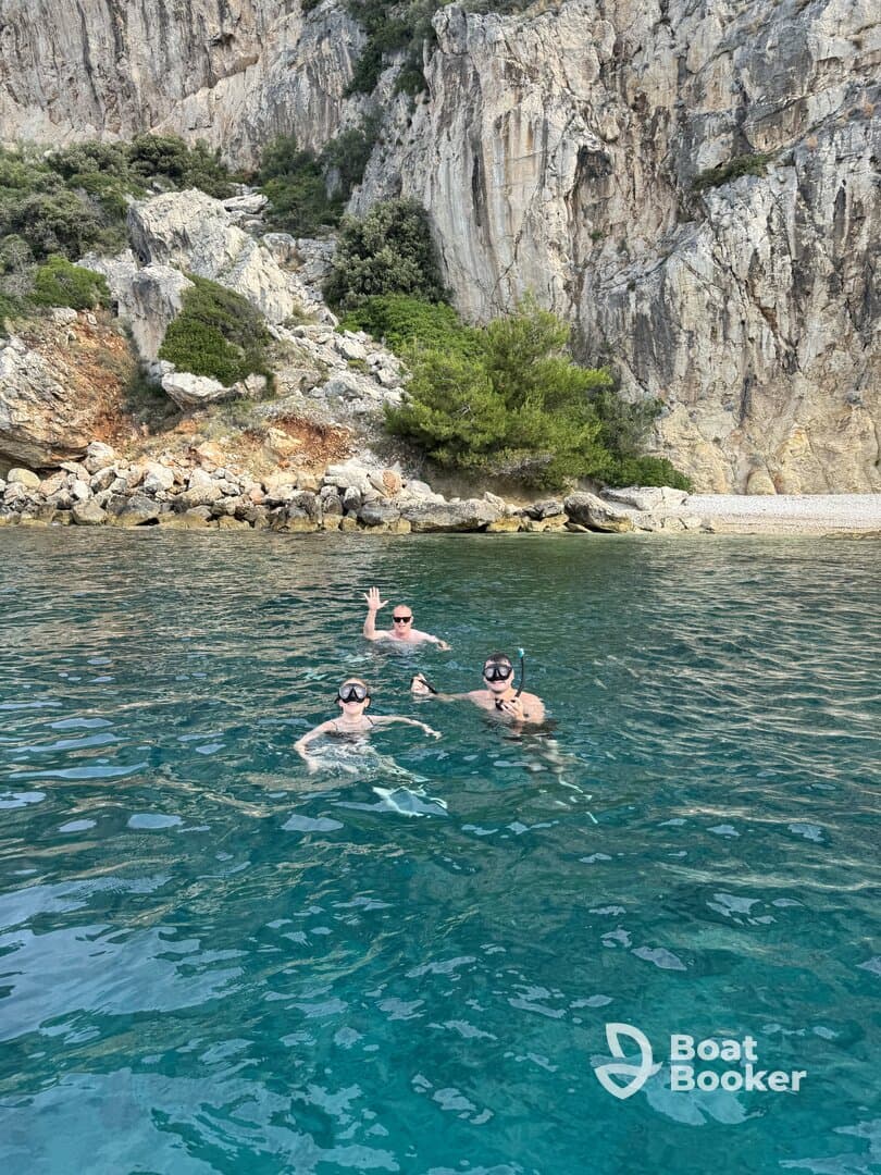 A group enjoys snorkeling in crystal-clear waters, surrounded by stunning rocky cliffs — a perfect adventure for water enthusiasts.