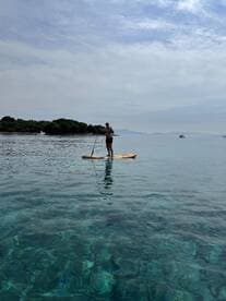A paddleboarder enjoys the serene waters, showcasing the beauty of clear turquoise depths — perfect for water sports enthusiasts.