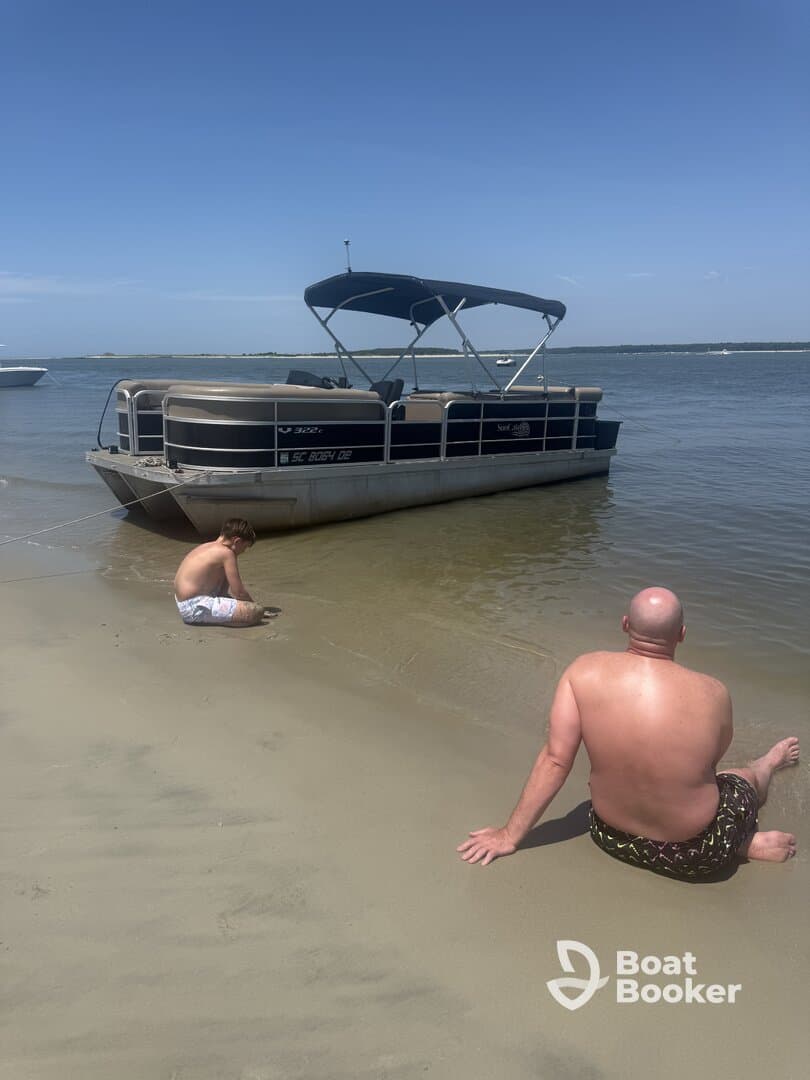 A family enjoys a relaxing day at the beach with a pontoon boat anchored nearby, perfect for sandbar stops and fun in the sun.