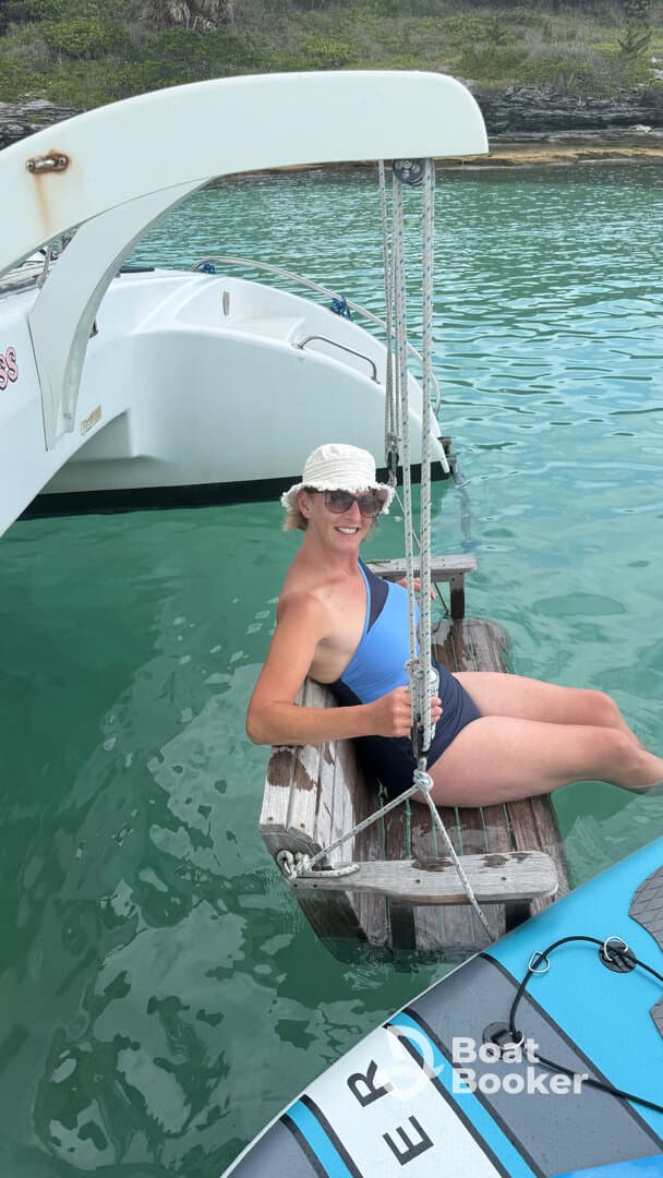 A woman enjoys a relaxing moment on a swing attached to a catamaran, surrounded by clear turquoise waters — perfect for a fun day on the water.