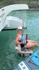 A woman enjoys a relaxing moment on a swing attached to a catamaran, surrounded by clear turquoise waters — perfect for a fun day on the water.