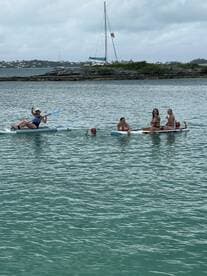 A lively group enjoys paddleboarding and swimming in clear waters, showcasing the fun of island hopping adventures.