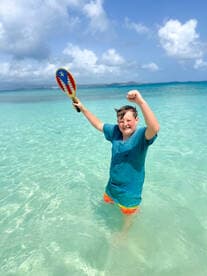 A joyful child celebrates in the shallow waters of a beautiful beach, showcasing the fun and excitement of a day in the sun.
