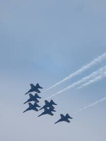 A formation of jets performing aerial maneuvers against a clear sky, showcasing precision flying.