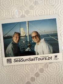 A couple enjoys a romantic sunset sailing experience, capturing a joyful moment on the water with the iconic backdrop of a bridge.