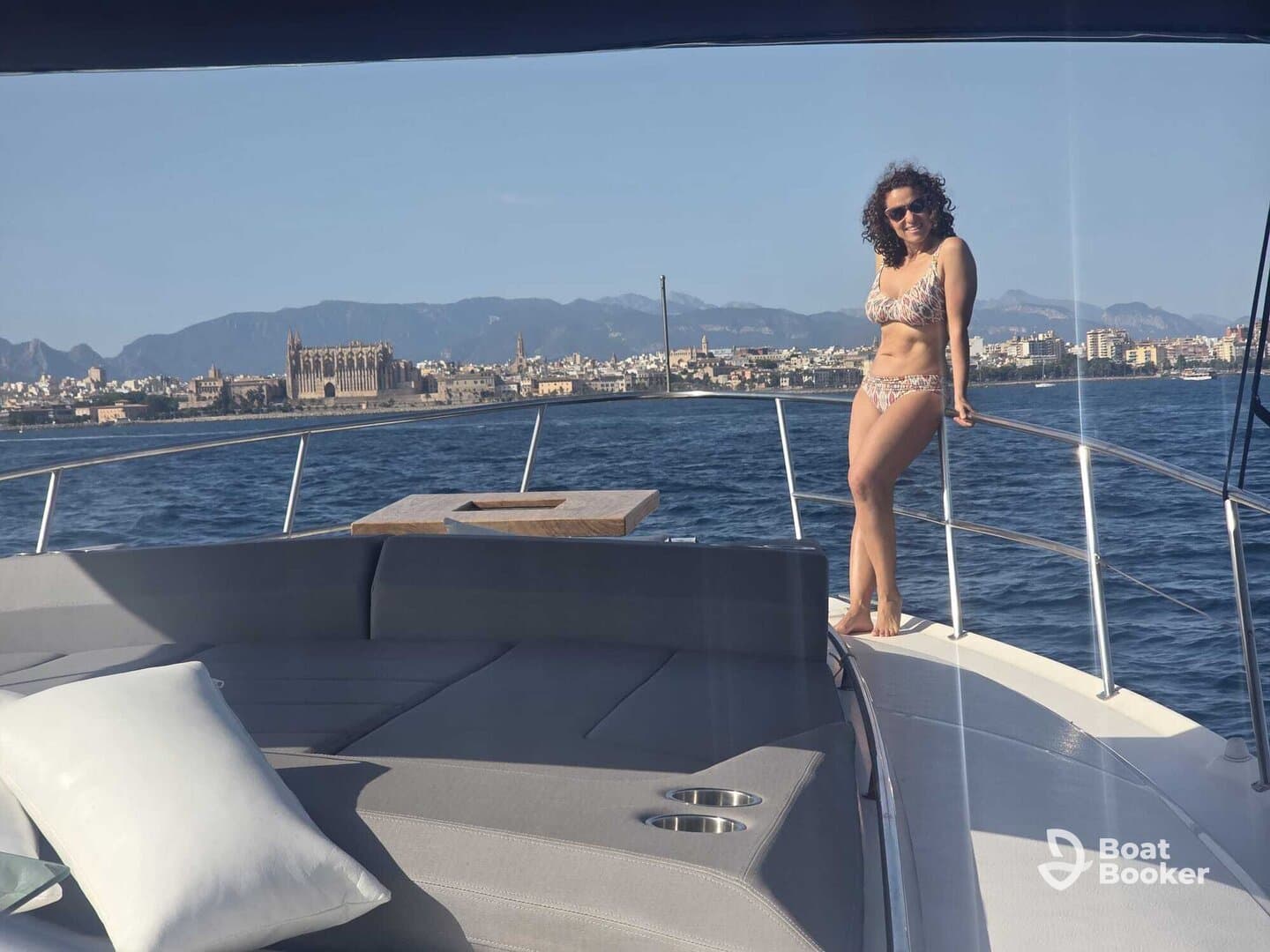 A woman poses on the bow of a yacht, enjoying the sunny weather and beautiful coastal scenery — a perfect moment for a day out on the water.