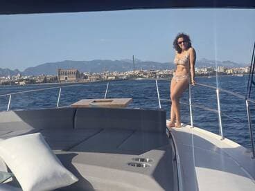 A woman poses on the bow of a yacht, enjoying the sunny weather and beautiful coastal scenery — a perfect moment for a day out on the water.