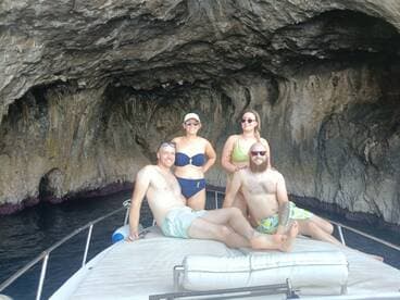 A cheerful group of friends relaxes on the deck of a boat near a stunning cave, enjoying their time on the water — perfect for memorable adventures and exploration.