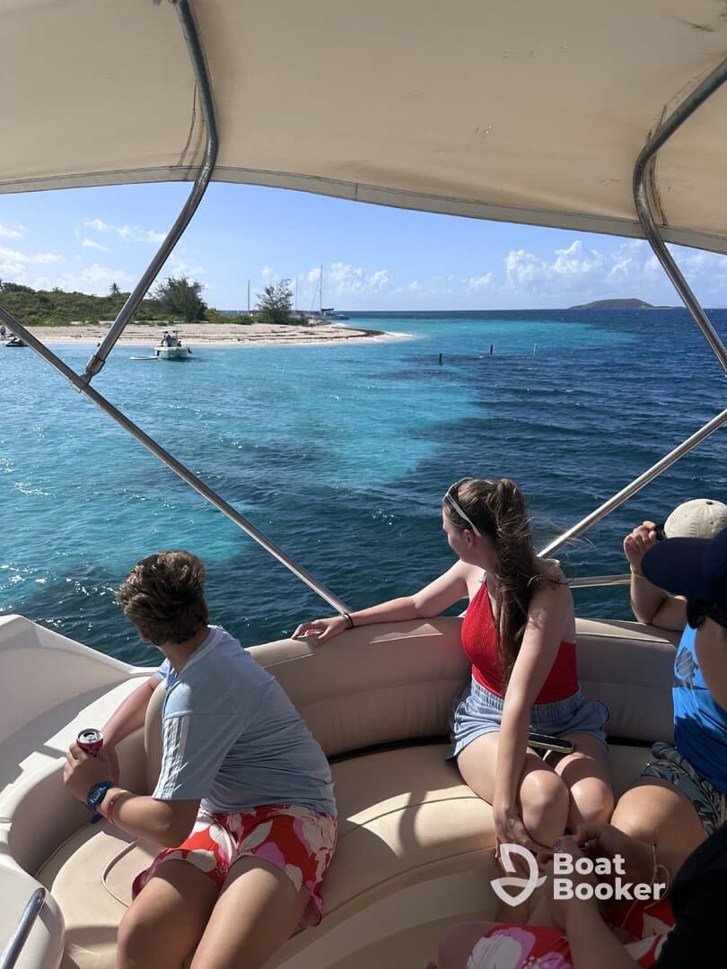 A group of friends enjoys a scenic view from their boat, looking towards a beautiful island and beach — perfect for a day of adventure on the water.