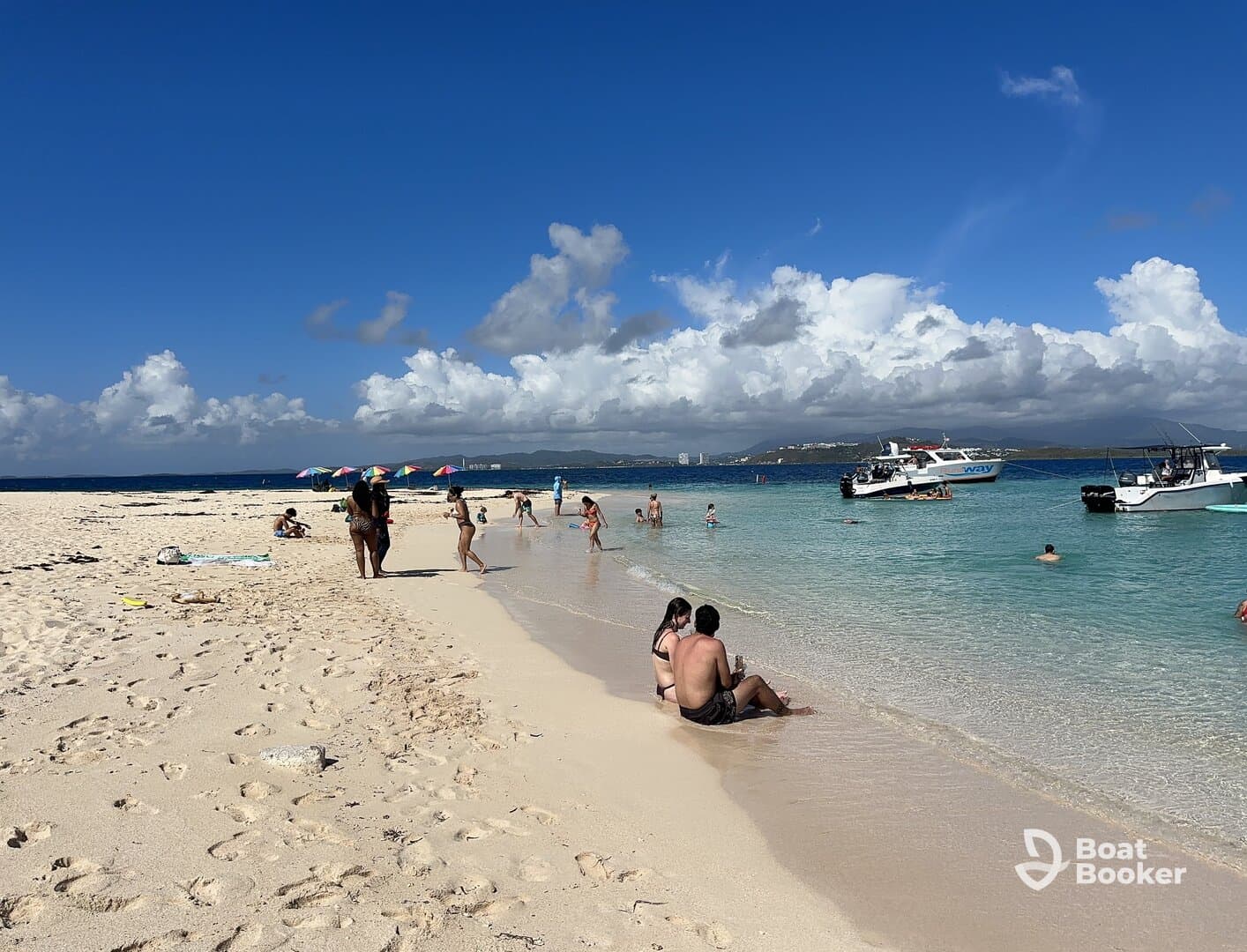 A lively beach scene with groups of people enjoying the sun and water, while boats are anchored nearby — perfect for a day of fun and relaxation on the shore.