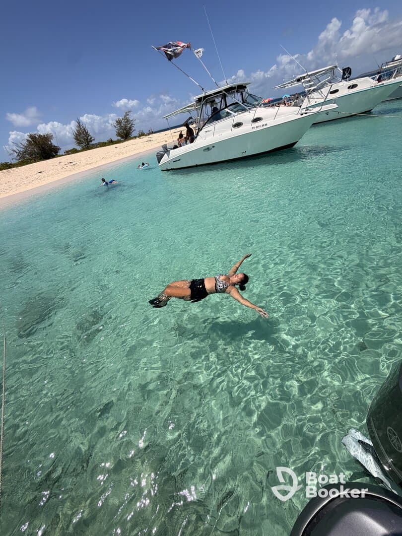 A woman enjoys a refreshing swim in crystal-clear waters near a boat, capturing the essence of a perfect beach day filled with fun and relaxation.