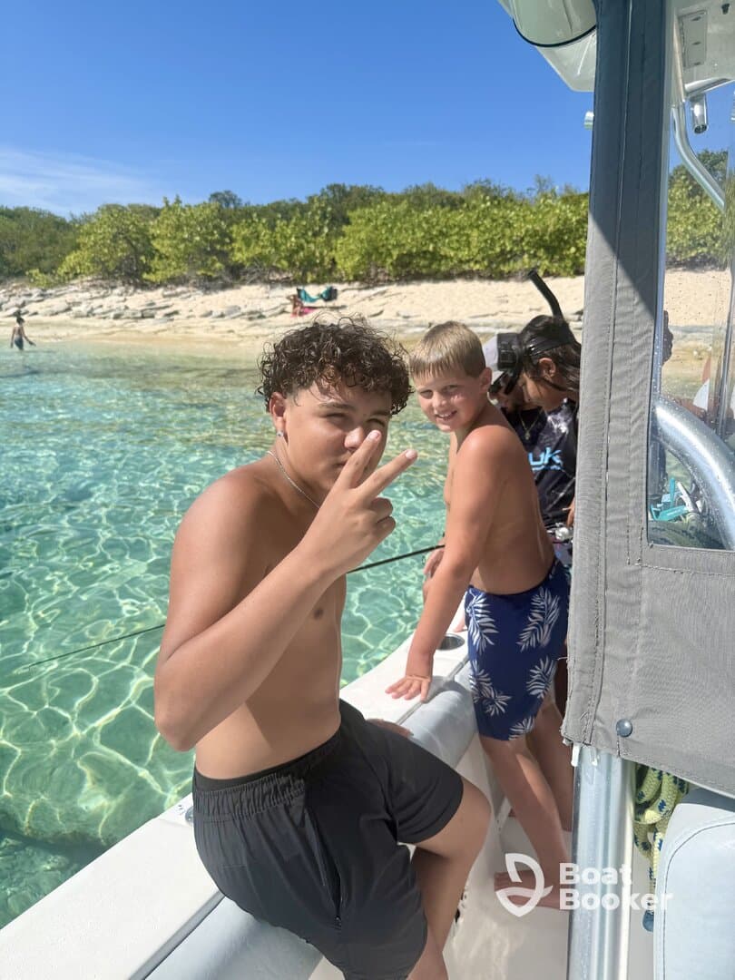 A group of kids enjoys a fun day on the water, posing on the edge of a boat with a beautiful beach backdrop — perfect for snorkeling adventures.