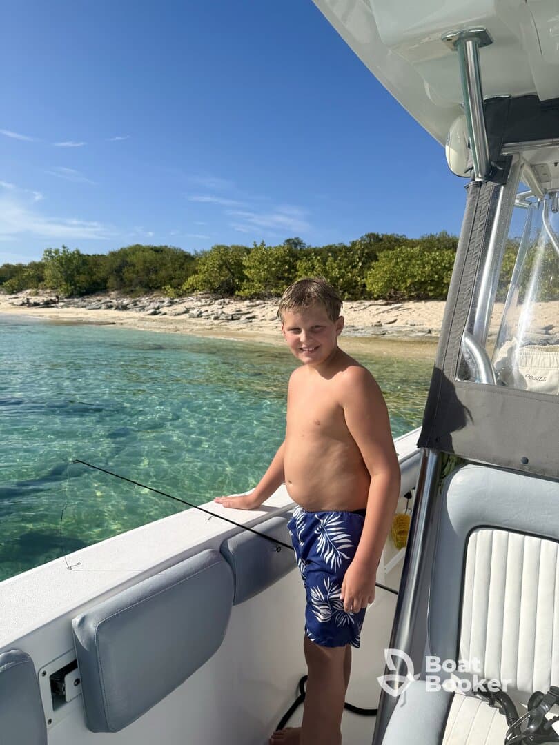 A young boy enjoys a fishing moment on a boat, surrounded by clear turquoise waters and a beautiful sandy beach backdrop — perfect for family adventures on the water.