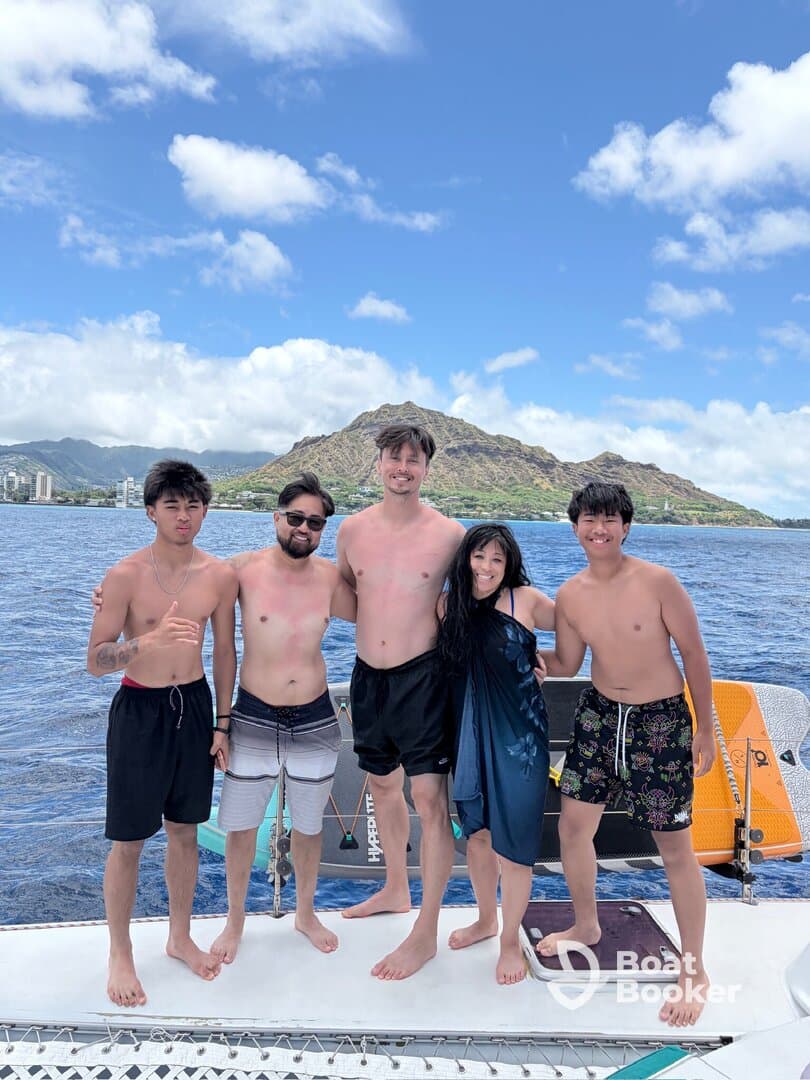 A joyful group of friends poses together on a boat, enjoying a sunny day on the water with stunning mountain views in the background — perfect for memorable beach outings.