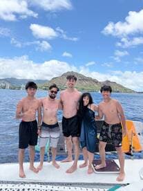 A joyful group of friends poses together on a boat, enjoying a sunny day on the water with stunning mountain views in the background — perfect for memorable beach outings.