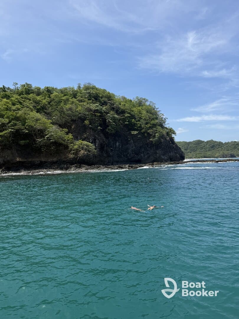 A couple enjoys a refreshing swim in the clear turquoise waters near a lush coastline, perfect for a relaxing day on the water.
