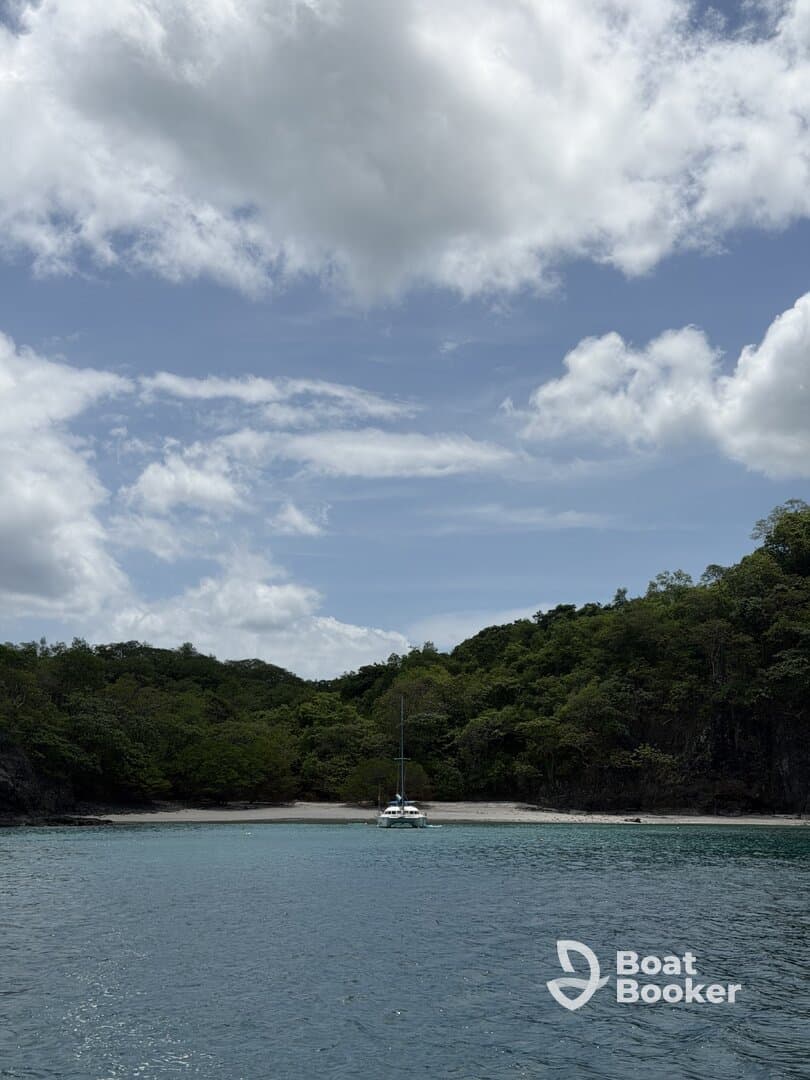 A serene view of a catamaran anchored in a secluded bay, surrounded by lush greenery and clear waters — an ideal spot for relaxation and exploration.