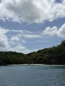 A serene view of a catamaran anchored in a secluded bay, surrounded by lush greenery and clear waters — an ideal spot for relaxation and exploration.