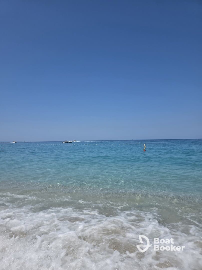 A serene view of a clear turquoise coastline with gentle waves lapping at the shore, perfect for a relaxing beach day.