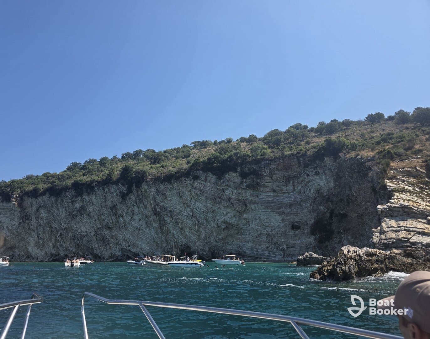 A stunning view of a rocky coastline with several boats anchored nearby, showcasing a vibrant day of swimming and exploration in crystal-clear waters.