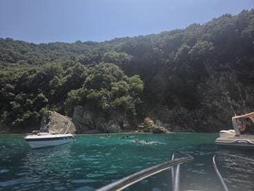 A lively scene of swimmers enjoying the clear waters near a rocky coastline, with boats anchored nearby, perfect for a day of fun and exploration.