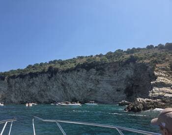 A stunning view of a rocky coastline with several boats anchored nearby, showcasing a vibrant day of swimming and exploration in crystal-clear waters.