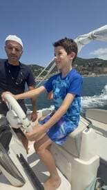 A child joyfully steers a boat under the guidance of an adult, capturing a memorable moment on the water — perfect for family adventures.