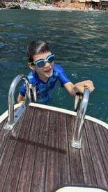 A joyful child climbs the ladder of a boat after swimming, showcasing the fun and excitement of water activities during a sunny day on the water.