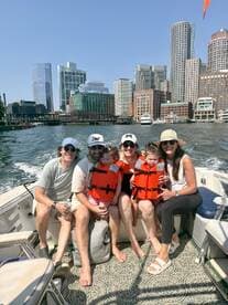 A joyful family enjoys a boat ride with a stunning city skyline in the background, all wearing life jackets for safety — a perfect day on the water.