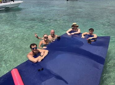 A lively group enjoys a fun day in the clear waters, relaxing on a floating mat and ready for snorkeling adventures.
