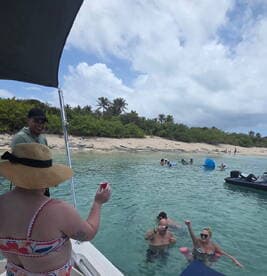 A lively group enjoys drinks and swimming in clear waters near a sandy beach, creating the perfect atmosphere for a fun day on the water.