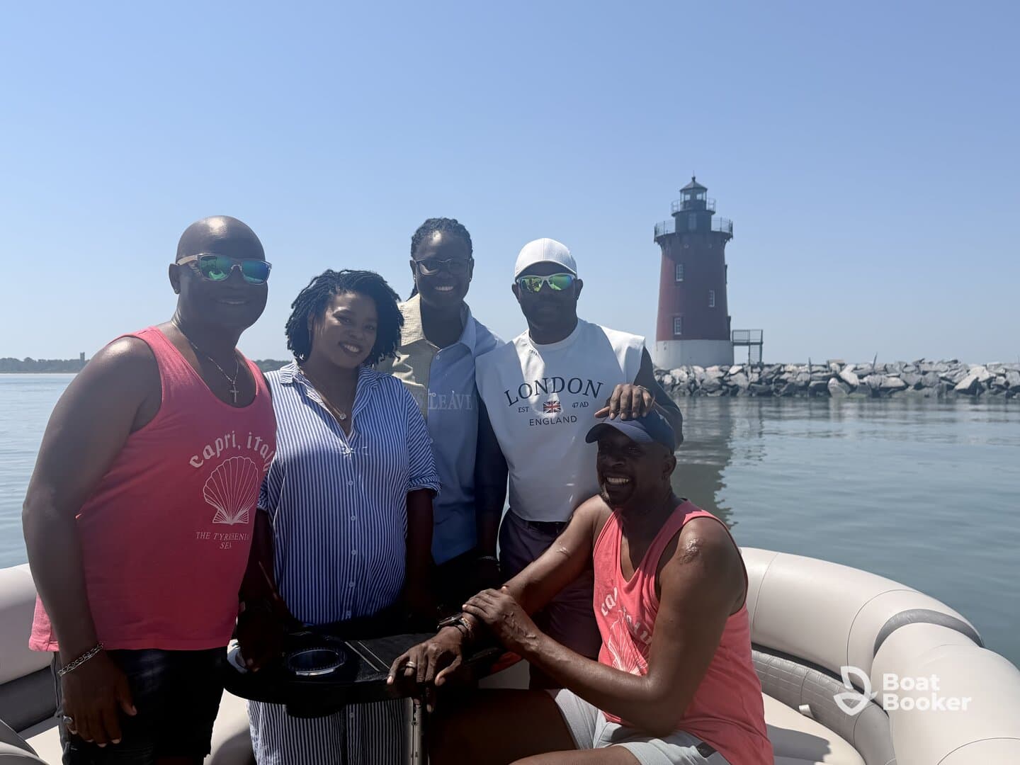 A cheerful group poses on a pontoon boat with a picturesque lighthouse in the background, capturing a memorable day on the water.