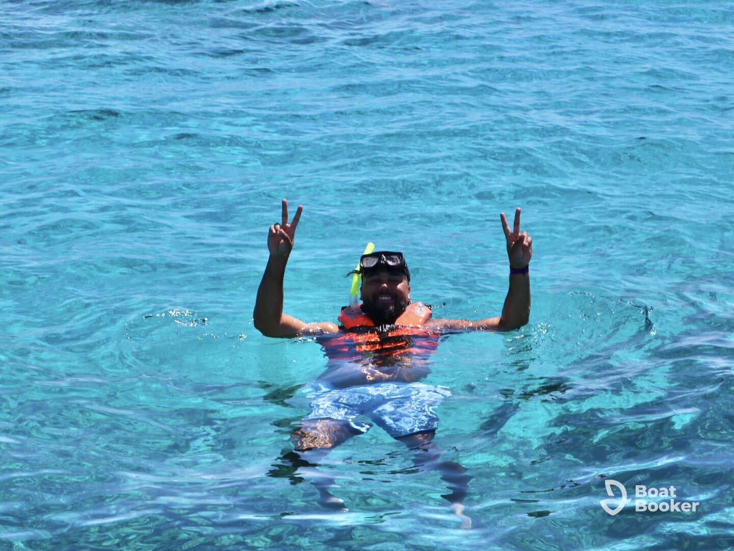 A snorkeler enjoys the vibrant turquoise waters, flashing a peace sign while floating — a perfect moment of fun and relaxation in the ocean.