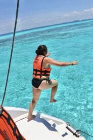 A woman in a life jacket prepares to jump into the stunningly clear waters, capturing the thrill of adventure on a sunny day at sea.