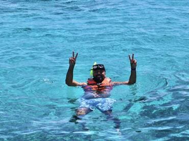 A snorkeler enjoys the vibrant turquoise waters, flashing a peace sign while floating — a perfect moment of fun and relaxation in the ocean.