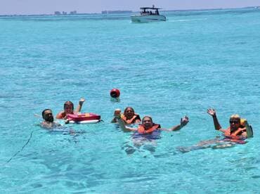 A lively group enjoys a refreshing swim in crystal-clear waters, celebrating with cocktails and laughter — the perfect backdrop for a fun day on the water.