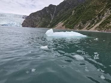 A stunning view of an iceberg floating in tranquil waters, with a backdrop of majestic glaciers and lush mountains, perfect for showcasing the beauty of nature.