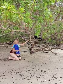A mother and child explore a beach, interacting with nature among the trees — a perfect family adventure in a tropical setting.