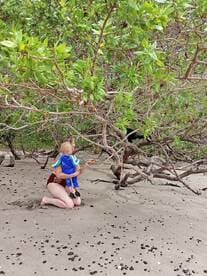 A mother and her child explore a sandy beach, surrounded by lush greenery — a perfect moment of family bonding in nature.