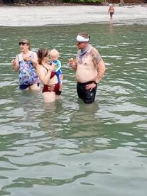 A family enjoys a fun day at the beach, wading in the water with drinks in hand — perfect for creating lasting memories during summer outings.
