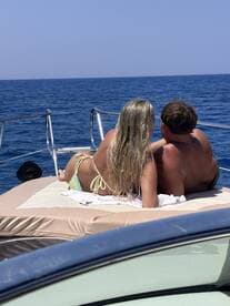 A couple enjoys a romantic moment sunbathing on the deck of a boat, surrounded by the serene blue ocean — perfect for a getaway or special occasion on the water.