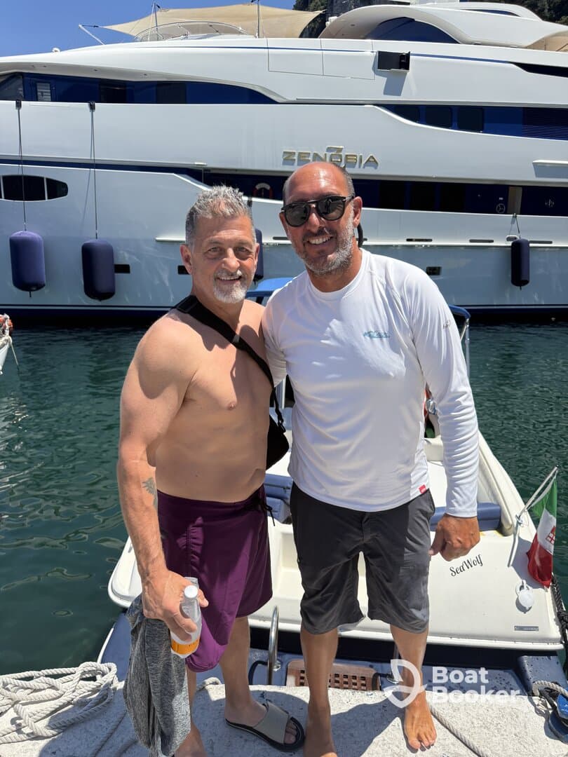 Two friends pose for a cheerful photo on the deck of a yacht, capturing a moment of celebration and camaraderie on the water.