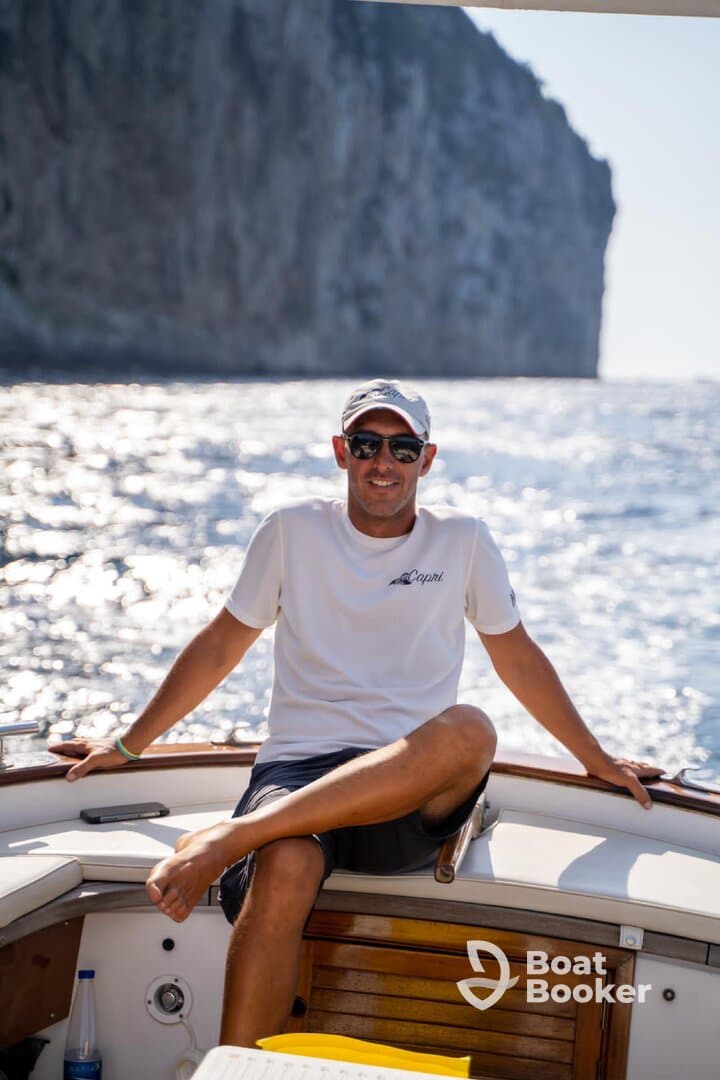 A man relaxes on the deck of a boat, enjoying the scenic ocean view near Capri — a perfect moment for sailing enthusiasts.