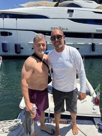 Two friends pose for a cheerful photo on the deck of a yacht, capturing a moment of celebration and camaraderie on the water.