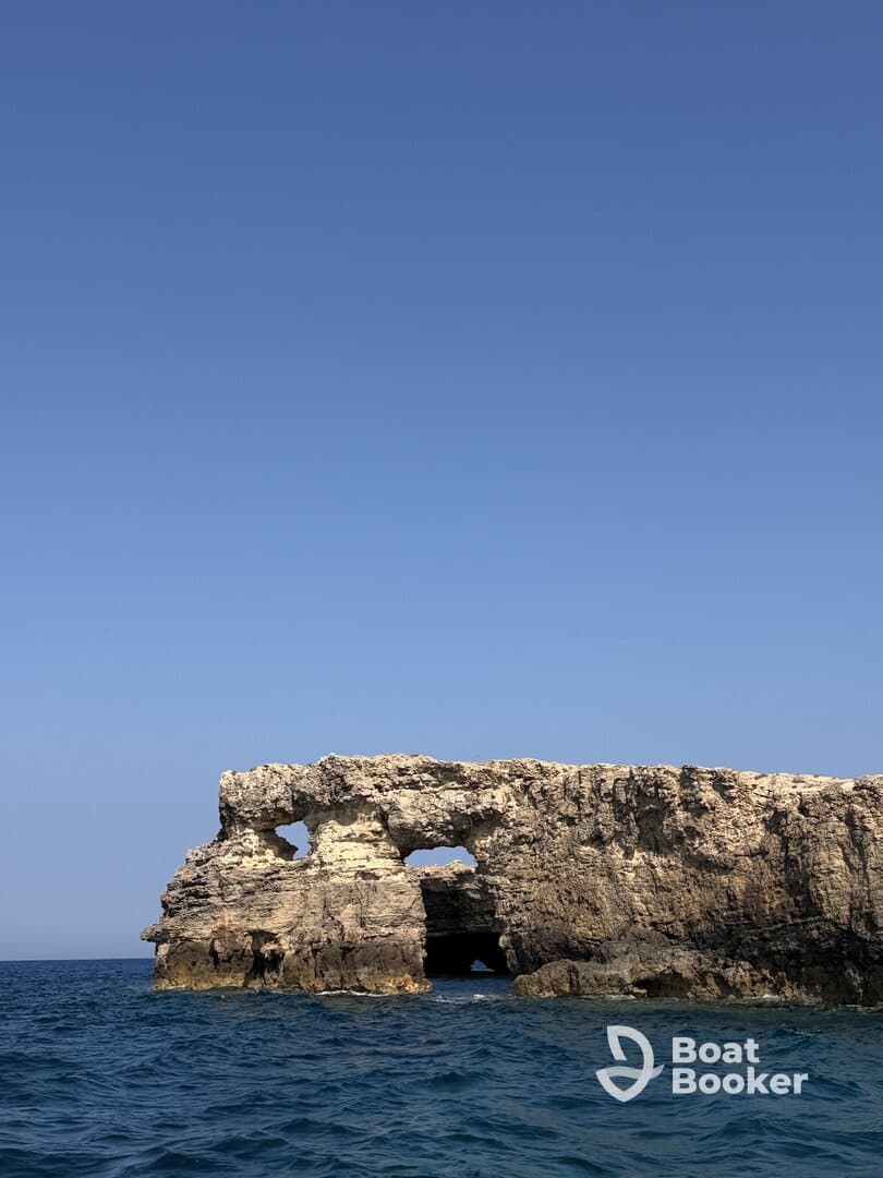 A stunning coastal rock formation stands majestically against a clear blue sky, perfect for scenic boat tours and exploration.